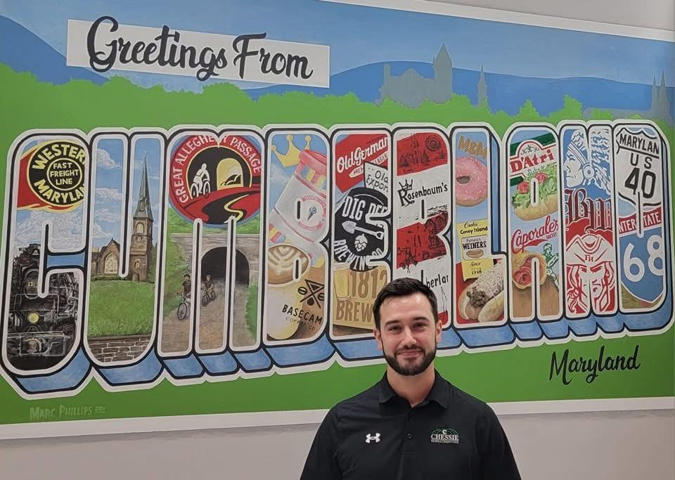 Marc Phillips standing in front of his Greetings from Cumberland mural